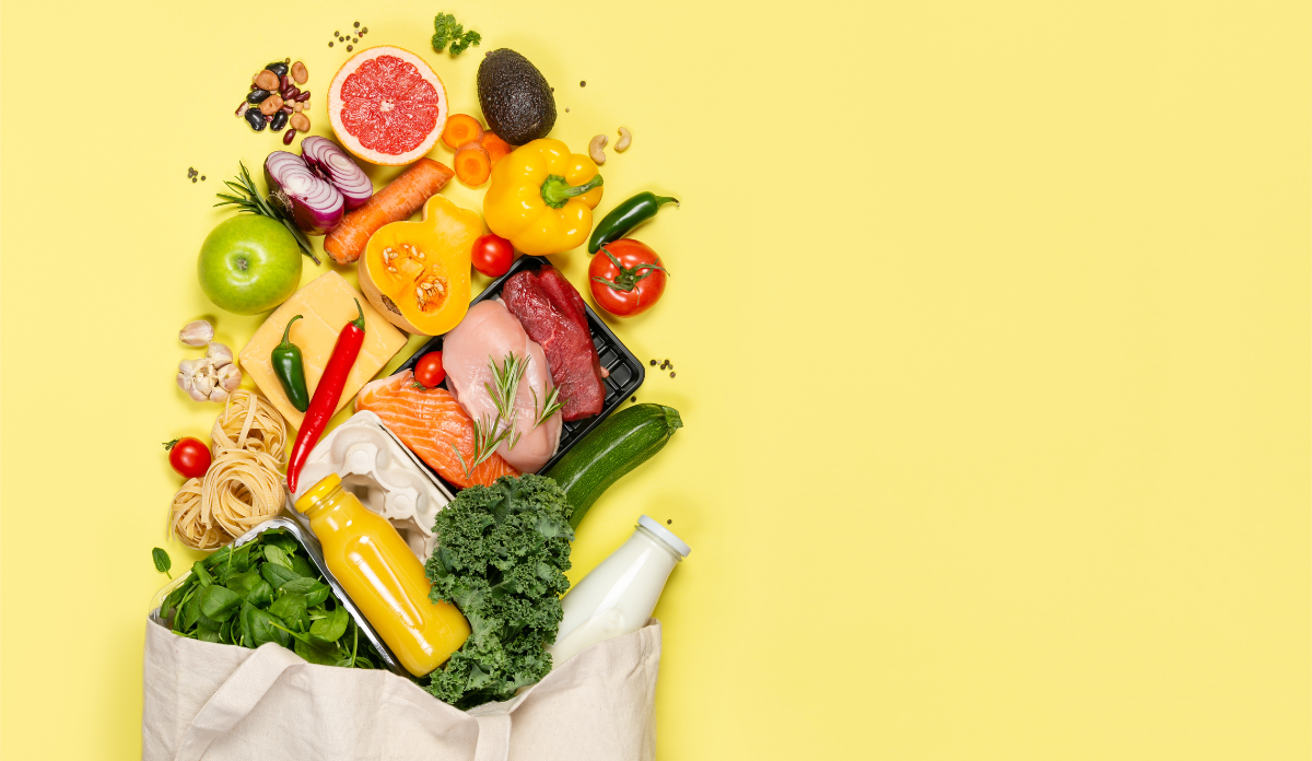 groceries and produce spilling out of a paper bag onto a yellow background